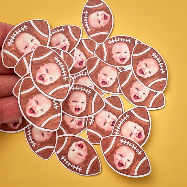 K&ouml;nnte beinhalten: Eine Ansammlung von Papierauschnitten in Form von Footballs, jeweils mit dem Gesicht eines l&auml;chelnden Babys. Die Footballs sind braun mit wei&szlig;en N&auml;hten, vor einem gelben Hintergrund.