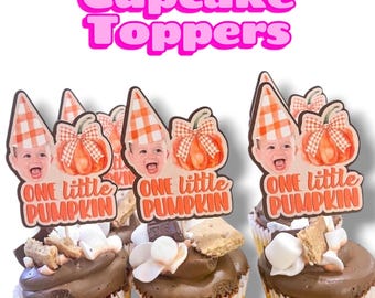 May include: Cupcake toppers featuring a baby's face wearing an orange and white checkered party hat next to a pumpkin with a matching bow. The text reads ONE little PUMPKIN in orange script and block letters on a white background.