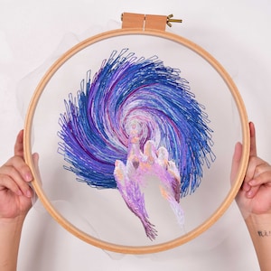 May include: A purple and blue embroidered design of a swirling galaxy with a hand reaching out from the center, framed in a wooden hoop.