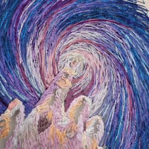 May include: A close-up of a swirling, embroidered design in shades of blue, purple, and pink. The design resembles a starry night sky with a large, swirling cloud in the center.