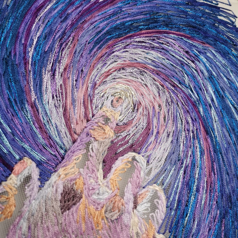 May include: A close-up of a swirling, embroidered design in shades of blue, purple, and pink. The design resembles a starry night sky with a large, swirling cloud in the center.
