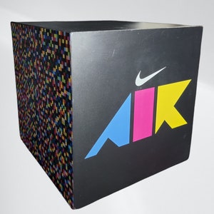 May include: A black cube with a colourful "AIR" logo and a white Nike swoosh. The cube is covered in a pixelated pattern.