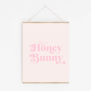 May include: A pink and white printable wall art print with the text "Honey Bunny" in a retro font. A small bunny ear graphic is above the text.