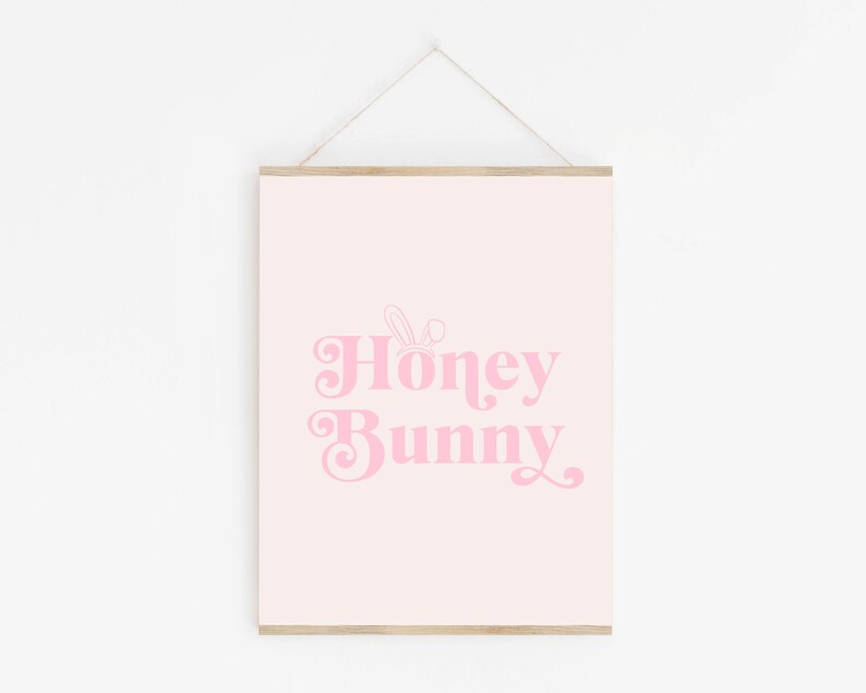 May include: A pink and white printable wall art print with the text "Honey Bunny" in a retro font. A small bunny ear graphic is above the text.