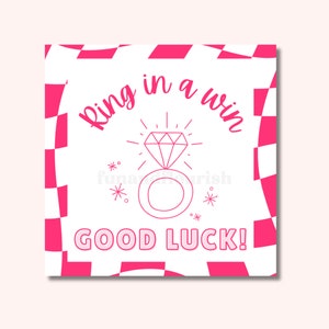 Puede incluir: Un fondo de cuadros rosa y blanco con una ilustración rosa de un anillo y un diamante. El texto "Ring in a win, good luck!" está escrito en rosa.