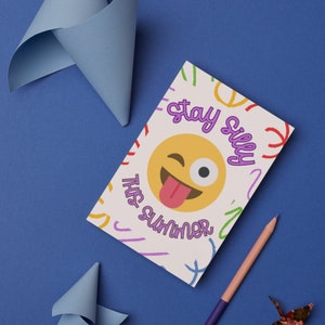 May include: A white card with a colorful background and the text "Stay Silly This Summer" in purple. A yellow cartoon face with a wink and tongue sticking out is in the center of the card.