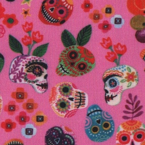 May include: Bright pink fabric with a repeating pattern of decorated sugar skulls, flowers, and other motifs. The skulls are in various colours, including red, blue, green, and orange, with detailed designs. Floral elements enhance the celebratory theme.