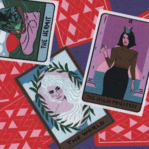 May include: A fabric design with tarot cards and red card backs on a purple backdrop. The tarot cards show illustrations of figures and include "The Hermit," "The Empress," and "The High Priestess." The red card backs have a diamond pattern.