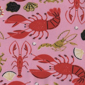 May include: Pink fabric featuring a repeating pattern of red lobsters, crabs, seashells, and black sea rocks. The lobsters and crabs are in a stylized design. The seashells are gold and white. The overall theme is nautical.