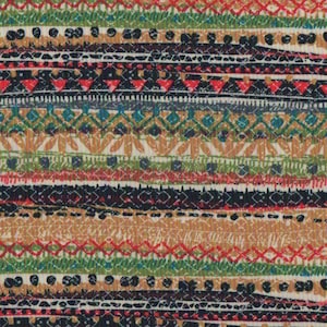 Op de afbeelding: Een kleurrijke stof met een herhalend patroon van strepen en geometrische ontwerpen in tinten rood, groen, blauw, zwart en bruin.