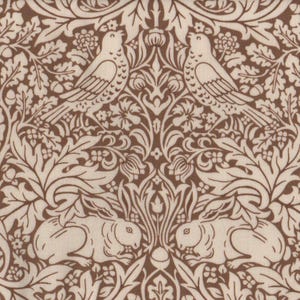 Op de afbeelding: Bruin en crèmekleurige stof met een herhalend patroon van vogels, konijnen en bladeren. Het ontwerp bevat gedetailleerde illustraties van vogels die tussen bladeren en eikels zitten, met konijnen eronder.