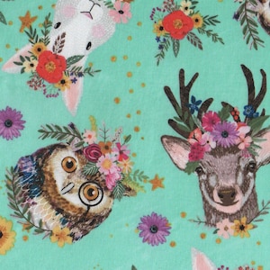 Puede incluir: Una tela turquesa con un patrón repetido de conejos blancos, búhos y ciervos que llevan coronas de flores. Los animales están rodeados de estrellas doradas y pequeños puntos blancos.