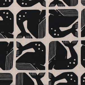Op de afbeelding: Een textielstof met een herhalend patroon van zwarte walvissilhouetten gedrukt op een lichtbeige achtergrond. Elke walvis is afgebeeld in een gestileerde blokdruk-esthetiek met zichtbare lijndetails op de vinnen en staartsecties.