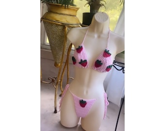May include: Pink crocheted bikini with strawberry accents. The top is a triangle style with adjustable straps. The bottom is a cheeky style with ties on the sides.