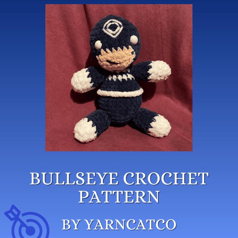 May include: A handmade crochet doll in a seated position. The doll is primarily navy blue with white accents on the hands, feet, and head. The face is tan with white eyes. The text "BULLSEYE CROCHET PATTERN" and "BY YARNCATCO" are displayed below the doll.