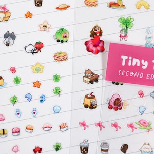 May include: Sheet of colorful Tiny Town Second Edition stickers. The stickers feature various cute illustrations, including food items, animals, and characters. The stickers are arranged on a white background with horizontal lines.