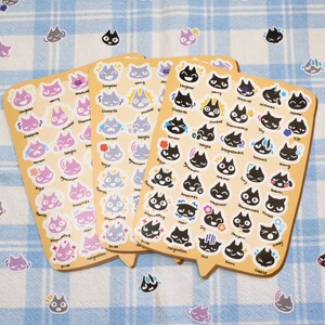 May include: Three sheets of stickers featuring black and white illustrations of cats with different emotions. The stickers are on a light blue and white checkered background. The emotions include: angry, sleepy, worried, shy, scared, happy, surprised, and more.
