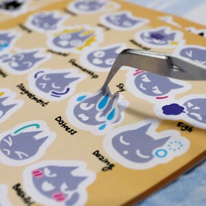 May include: A set of gray cat stickers with different facial expressions and emotions. Each sticker has a word describing the emotion, such as "sorry", "distress", "shy", and "sigh".