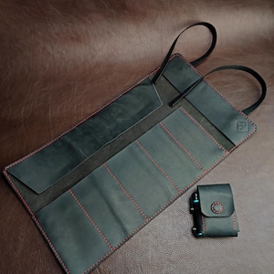 以下が含まれることがあります： 赤いステッチと複数のポケットが付いた黒い革製のロールアップケース。ケースは、工具やその他の小さなアイテムを収納するために設計されています。ボタン留めのある小さな黒い革製のポーチも含まれています。