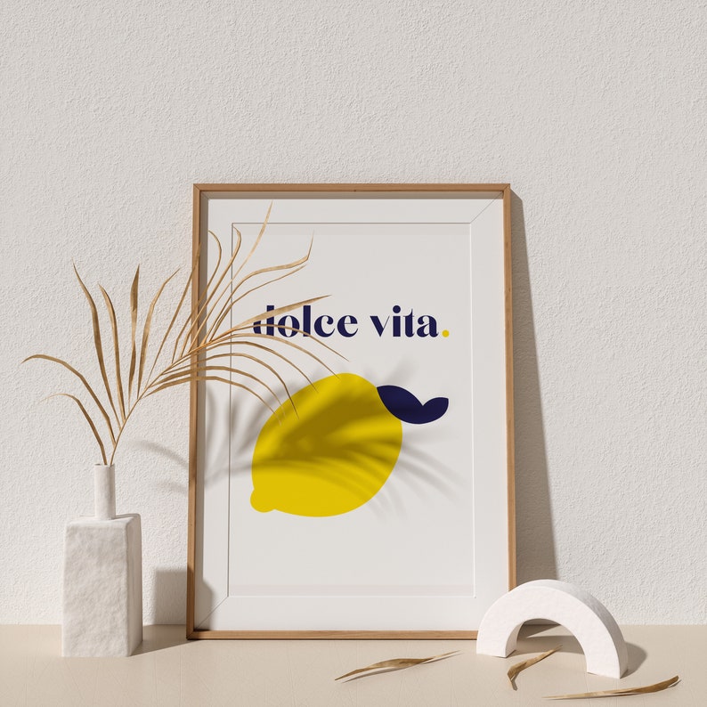 Puede incluir: Una impresi&oacute;n art&iacute;stica enmarcada con una ilustraci&oacute;n de lim&oacute;n amarillo y las palabras "dolce vita" en azul marino. La impresi&oacute;n est&aacute; en un marco de madera. La imagen tambi&eacute;n muestra un jarr&oacute;n blanco con hojas secas y un arco decorativo blanco.