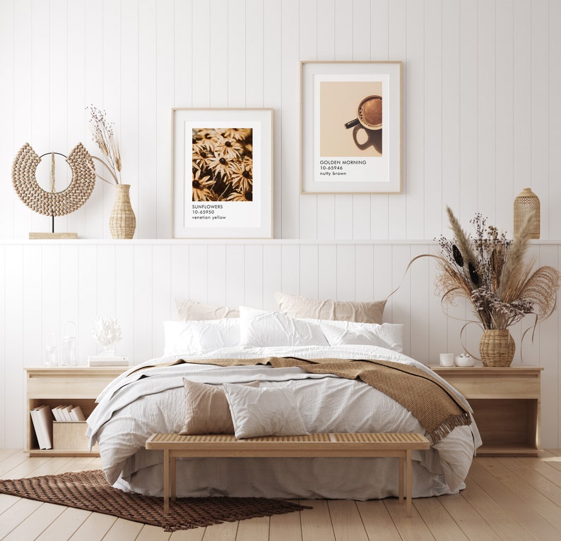 May include: A white bed with a brown blanket and a wooden bench in front of it. There are two framed prints on the wall behind the bed, one with a sunflower image and the other with a coffee cup image. The text on the prints reads "Sunflowers 10-43950 vermillion yellow" and "Golden Morning 10-45946 nutty brown".