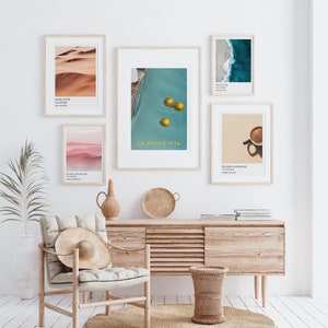 May include: A living room interior with a wooden console table and a chair. The wall is decorated with framed prints featuring a desert landscape, a pool with lemons, a beach scene, a mountain range, and a cup of coffee. The text on the prints reads "Sand Dune 10.45948", "La Dolce Vita", "Salted Air 10.45948", "Misty Landscapes 10.45948", and "Golden Morning 10.45948".
