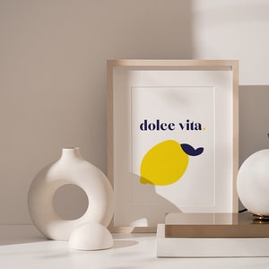 Puede incluir: Una impresi&oacute;n art&iacute;stica enmarcada con las palabras "dolce vita" y una ilustraci&oacute;n de lim&oacute;n amarillo. La impresi&oacute;n se muestra sobre una superficie blanca con jarrones decorativos y una l&aacute;mpara esf&eacute;rica. La paleta de colores incluye blanco, amarillo, azul y beige.