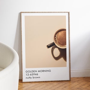 May include: A framed poster with a photo of a cup of coffee with a brown background. The text on the poster reads "GOLDEN MORNING 12-65946 nutty brown".