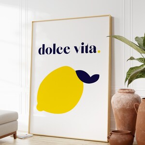 Puede incluir: Un cuadro enmarcado con una ilustraci&oacute;n de un lim&oacute;n amarillo y la frase "dolce vita" en azul marino. La obra de arte est&aacute; en un marco dorado. Una elegante pieza de arte mural para la cocina o el sal&oacute;n.
