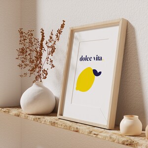 Puede incluir: Una impresi&oacute;n art&iacute;stica enmarcada con un lim&oacute;n amarillo y una hoja azul, y las palabras "dolce vita". La impresi&oacute;n est&aacute; en un marco de madera clara, exhibida en un estante de madera con un jarr&oacute;n blanco y peque&ntilde;as macetas de cer&aacute;mica.