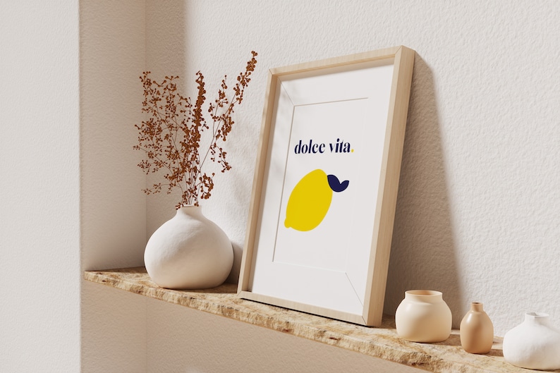 Puede incluir: Una impresi&oacute;n art&iacute;stica enmarcada con un lim&oacute;n amarillo y una hoja azul, y las palabras "dolce vita". La impresi&oacute;n est&aacute; en un marco de madera clara, exhibida en un estante de madera con un jarr&oacute;n blanco y peque&ntilde;as macetas de cer&aacute;mica.