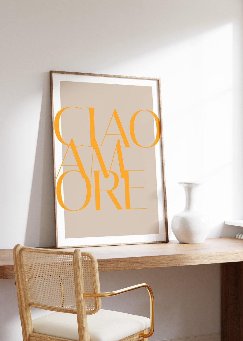 May include: A framed print with the text "CIAO AMORE" in orange on a beige background. The print is hanging on a wall above a wooden desk with a chair.