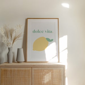 May include: A framed print with a yellow lemon and the text "dolce vita." The print is hanging on a white wall above a light brown cabinet with a woven rattan front.