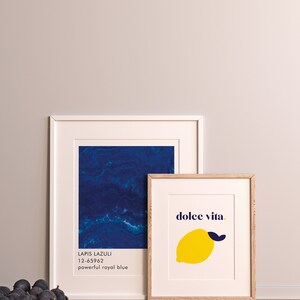 Puede incluir: Dos impresiones art&iacute;sticas enmarcadas. Una presenta un dise&ntilde;o abstracto azul profundo con el texto "Lapis Lazuli 12-65962 powerful royal blue". La otra impresi&oacute;n tiene una ilustraci&oacute;n de lim&oacute;n amarillo con las palabras "dolce vita."