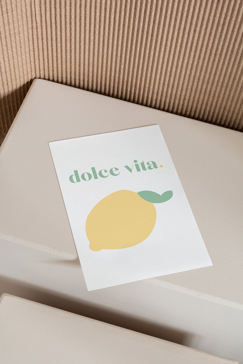 May include: A white card with the text "dolce vita." printed in green. A yellow lemon with a green stem is illustrated below the text.