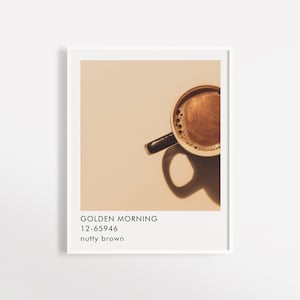 May include: A close-up of a cup of coffee with a light brown background. The coffee is a dark brown color and has a creamy foam on top. The text "GOLDEN MORNING 12-65946 nutty brown" is below the cup.