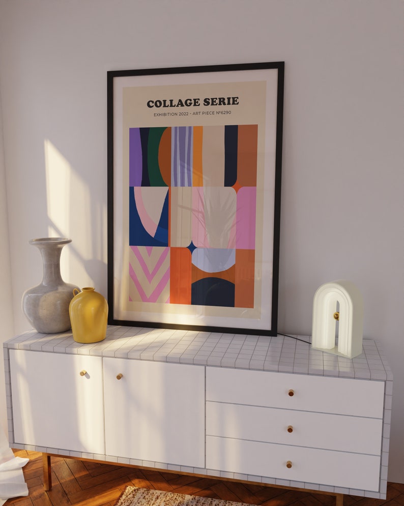 Op de afbeelding: Een ingelijste kunstprint getiteld "COLLAGE SERIE" met een abstract ontwerp in diverse kleuren, waaronder blauw, roze en oranje. De print wordt getoond boven een witte kast met gouden knoppen, samen met een decoratieve lamp en vazen.