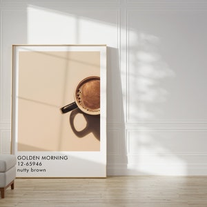 May include: A framed print of a coffee cup with a light brown background. The text on the print reads "GOLDEN MORNING 12-65946 nutty brown".