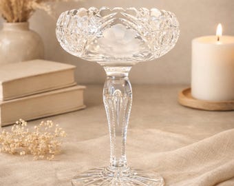 Peut inclure: Une coupe sur pied en verre transparent dotée d'un bord festonné, de motifs en diamant taillés et d'un motif floral givré central. La coupe repose sur un pied fin et facetté relié à une large base circulaire aux gravures linéaires rayonnantes.