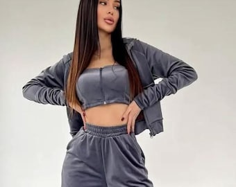 May include: A three-piece gray velour tracksuit set. The set includes a zip-up jacket, a tube top, and wide-leg pants. The outfit is made of a soft, plush fabric and is paired with white sneakers. The model is standing in front of a white background.