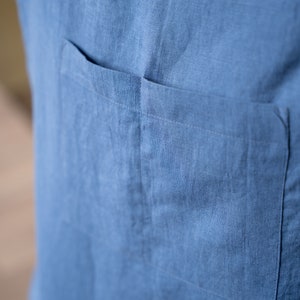 May include: A close-up of a blue linen shirt with a single patch pocket on the left side.