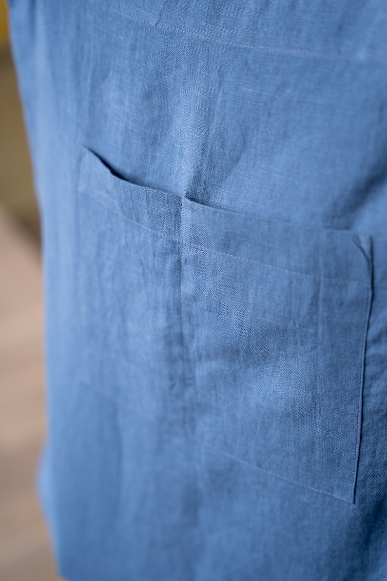 May include: A close-up of a blue linen shirt with a single patch pocket on the left side.