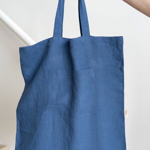 May include: A blue linen tote bag with a small pocket on the front. The bag has two long handles.