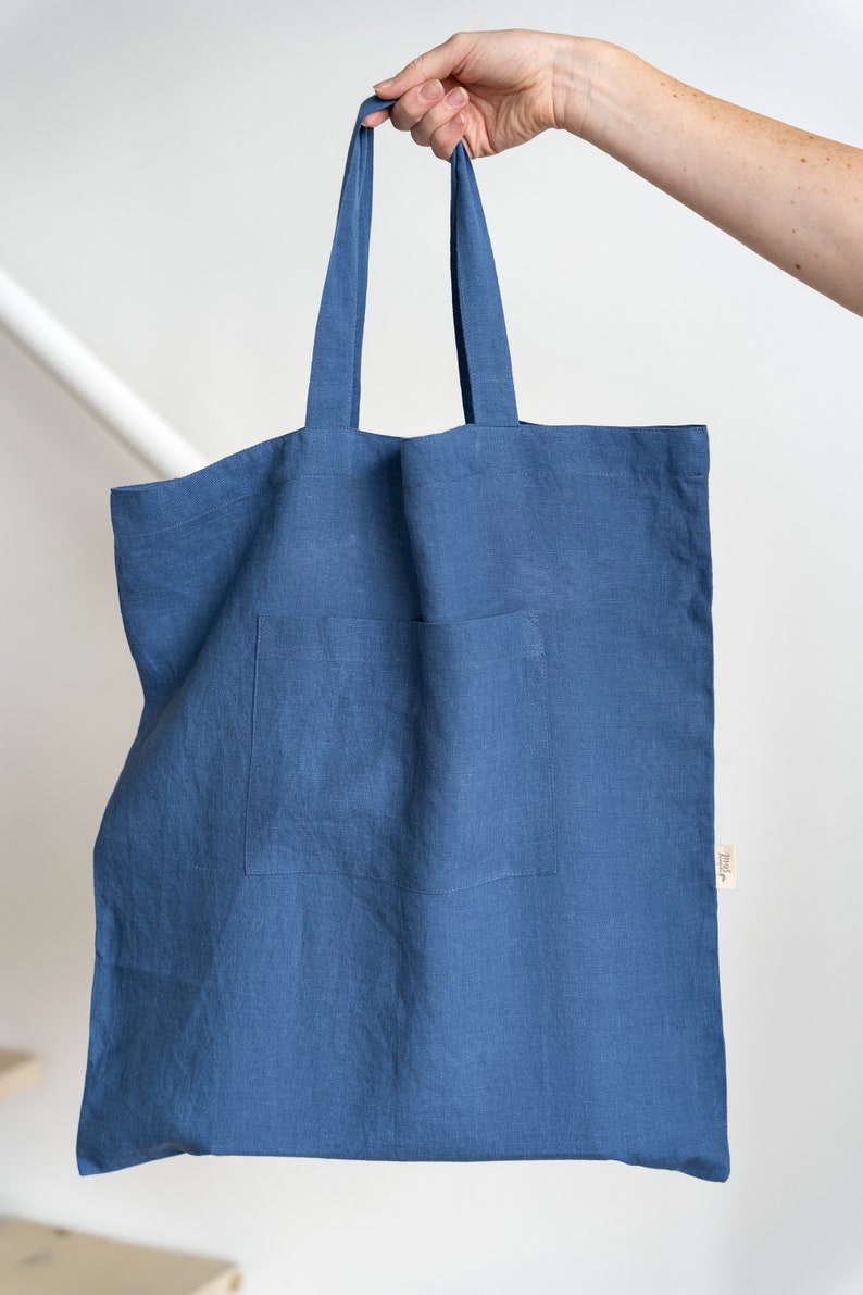 May include: A blue linen tote bag with a small pocket on the front. The bag has two long handles.