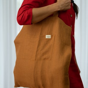 May include: A brown linen tote bag with a large pocket on the front. The bag has a small brown leather tag with the text "The Happy Soul" on it.
