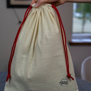 May include: A white drawstring bag with red drawstrings and a black logo that says "my own soul".