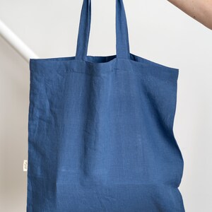 May include: A blue linen tote bag with two handles. The bag is empty and held by a hand.