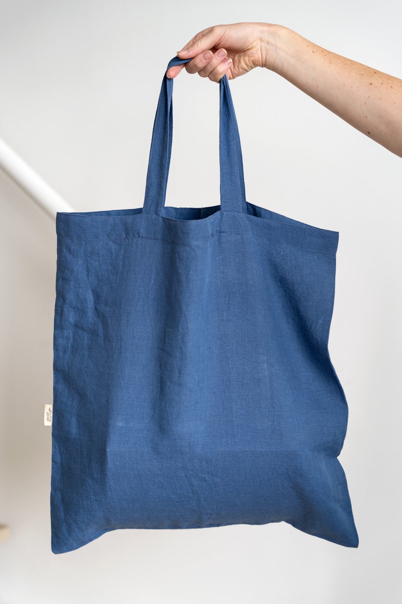 May include: A blue linen tote bag with two handles. The bag is empty and held by a hand.