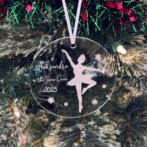 May include: A clear round Christmas ornament with a white silhouette of a ballerina with the text "Aleksandra as the Snow Queen 2023"