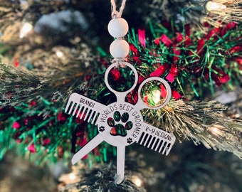 May include: White wooden ornament shaped like a pair of scissors and combs with the text "World's Best Groomer" and "K-9 Designs". The ornament is personalized with the name "Brandi".